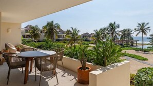 A balcony with a table and chairs, overlooking a beach with palm trees and a resort in the background. - Zihuatanejo 3BR • Sunset Views, Pool + Beach Acces (Zihuatanejo)