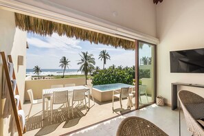 Een balkon met een zwembad, witte meubels en uitzicht op de oceaan en palmbomen.
