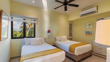 Habitación de hotel con dos camas, ventilador de techo, unidad de aire acondicionado y ventana con vista a palmeras.
