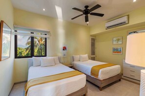 A hotel room with two beds, a ceiling fan, an air conditioning unit, and a window with a view of palm trees. - 1BR Boutique Villa • Pool + Beach Access (Zihuatanejo)
