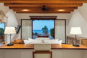 A hotel room with a large window offering a view of the ocean, a wooden ceiling, and a desk with a lamp. - 4BR Villa Playa Blanca – Infinity Views & Comfort (Zihuatanejo)