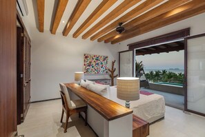 A modern bedroom with a wooden ceiling, a bed with a white cover, a desk with a lamp, and a view of the ocean through large glass doors. - 4BR Villa Playa Blanca – Infinity Views & Comfort (Zihuatanejo)