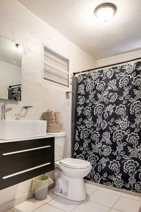Un baño con lavamanos blanco, inodoro y cortina de ducha con estampado floral.