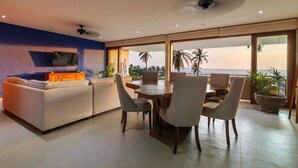 A modern living room with a sofa, dining table, and chairs, a television, and a view of the ocean. - 3BR Villa I Breathtaking Ocean Views + Terrace (Zihuatanejo)