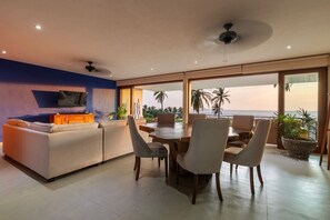 A modern living room with a sofa, dining table, and chairs, a television, and a view of the ocean. - 3BR Villa I Breathtaking Ocean Views + Terrace (Zihuatanejo)