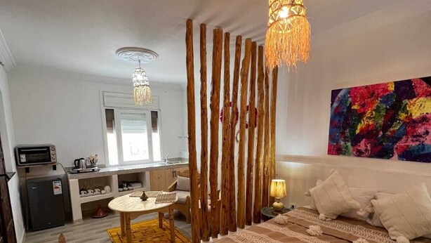 A hotel room with a bed, a dining table, a kitchen area, and a colorful abstract painting on the wall. - Sun & surf studio (Tamraght)