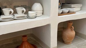 A kitchen area with white shelves holding various white ceramic dishes and a terracotta pot. - Sun & surf studio (Tamraght)