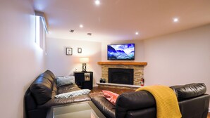 Uma sala de estar com lareira, televisão montada acima e sofá de couro.