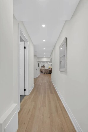 A hallway with white walls and wooden flooring leading to a dining area with a table and chairs.