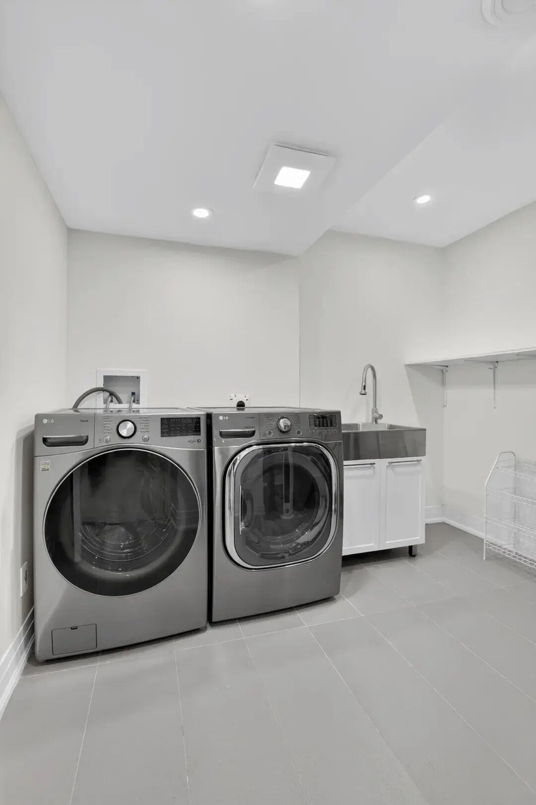 A laundry room with two front-loading washing machines, a sink, and a drying rack.