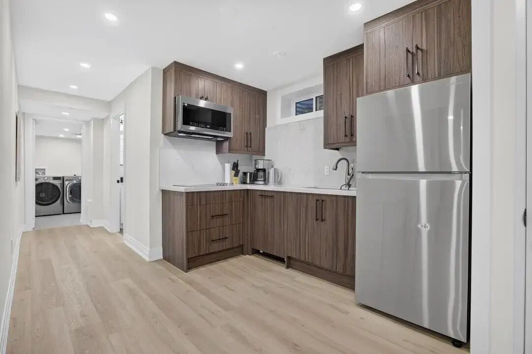 Una cocina moderna con armarios de madera, electrodomésticos de acero inoxidable y una lavadora a la vista en el fondo.