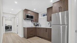 Une cuisine moderne avec des meubles en bois, des appareils électroménagers en acier inoxydable et un lave-linge visible au fond.