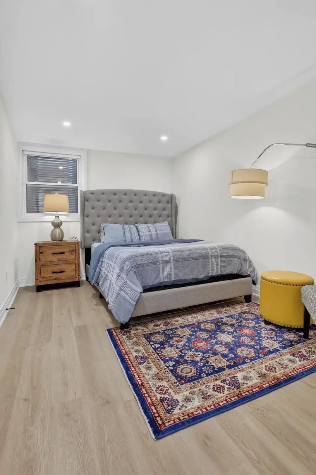 A bedroom with a bed, a nightstand, a lamp, a rug, and a wall-mounted light fixture.