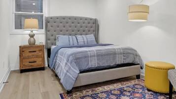 A bedroom with a bed, a nightstand, a lamp, a rug, and a wall-mounted light fixture.