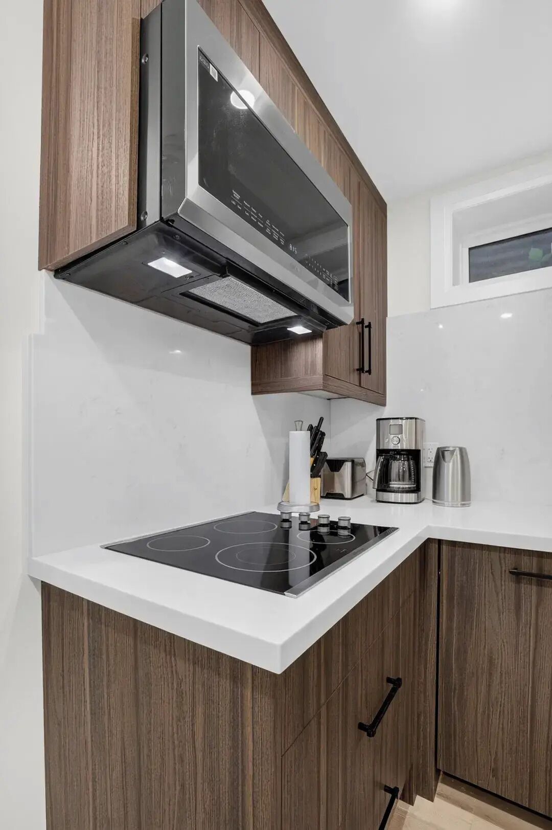 Een moderne keuken met een inbouwfornuis, koffiezetapparaat en houten kastjes.