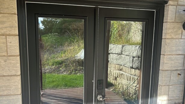 Una puerta doble negra con teclado electrónico, ubicada en una pared de piedra y con una cubierta de madera al frente.