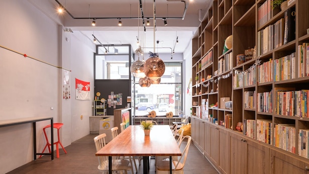 A modern library with a wooden table, chairs, and bookshelves filled with books. - Dumbo Hostel Hualien (Hualien City)
