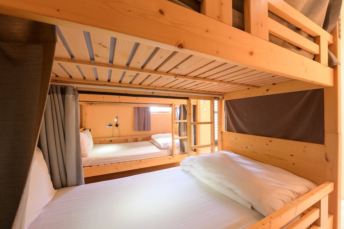 A wooden cabin with bunk beds, a small window, and curtains.