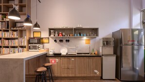 A modern kitchen with wooden cabinets, a built-in microwave, a refrigerator, and a coffee machine. There are two bar stools and a shelf with kitchenware. - Dumbo Hostel Hualien (Hualien City)