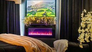 A cozy room with a fireplace, a television displaying a scenic landscape, and a comfortable seating area. - Perfectly Romantic in Branson Charming 1-bedroom condo-Jacuzzi Tub-No Stairs (Branson)