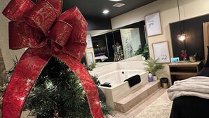 A hotel room with a large red bow on a Christmas tree, a bathtub, and a mirror reflecting the room. - Perfectly Romantic in Branson Charming 1-bedroom condo-Jacuzzi Tub-No Stairs (Branson)