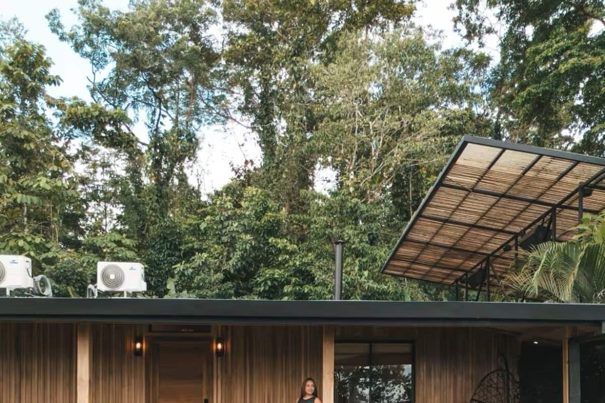 A modern house with a wooden exterior, a covered porch, and a garden with tropical plants.