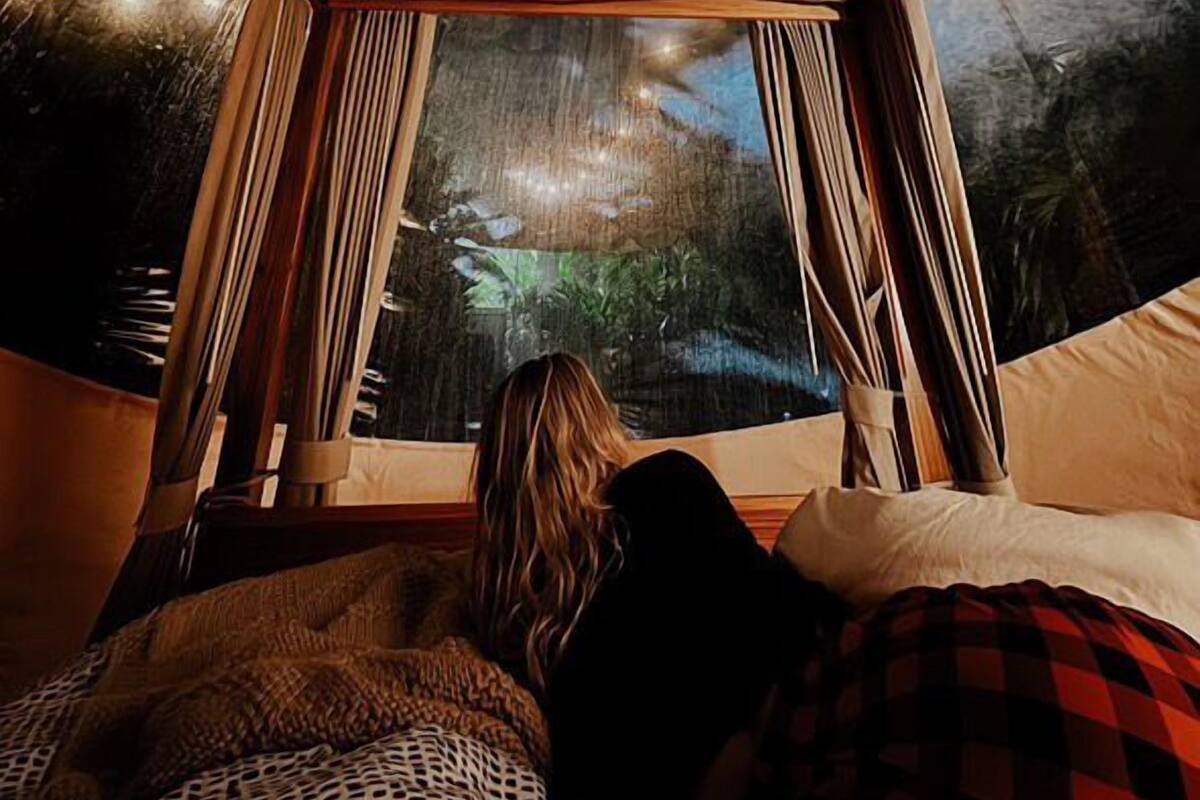 A cozy room with a canopy bed, a view of the outdoors, and a rustic ceiling.