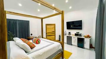 Een moderne slaapkamer met een hemelbed, een flatscreen televisie, een kleine kitchenette en een badkamer met douchegordijn.