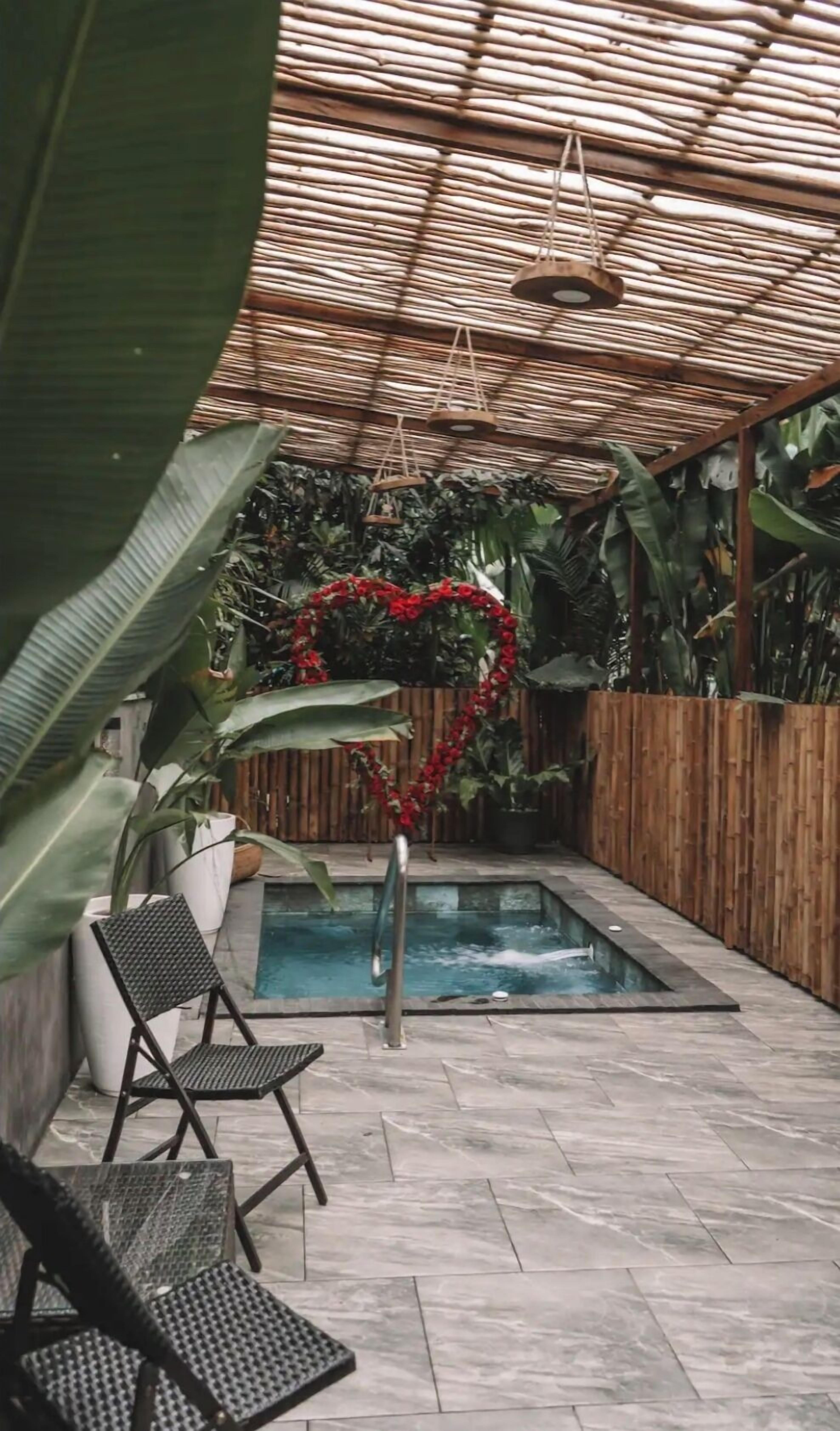 An outdoor pool area with a heart-shaped decoration, surrounded by potted plants and a bamboo fence.