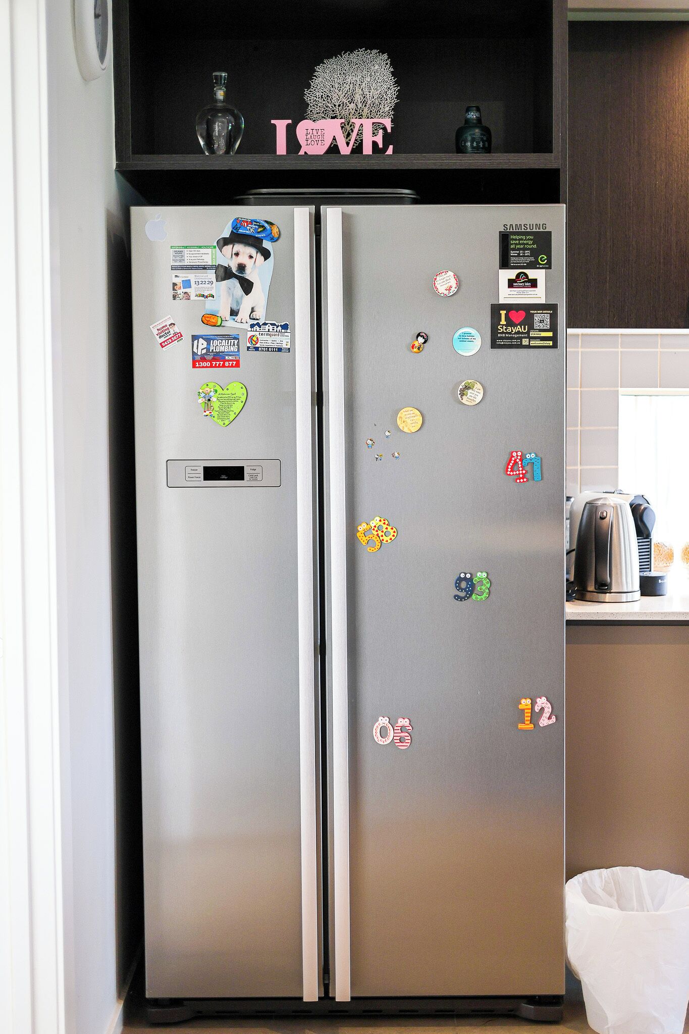 A stainless steel refrigerator with various magnets and stickers, including a heart-shaped one and a number four.