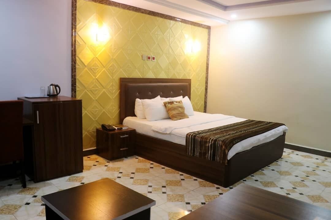 A hotel room with a large bed, a wooden nightstand, a desk, and a wardrobe.