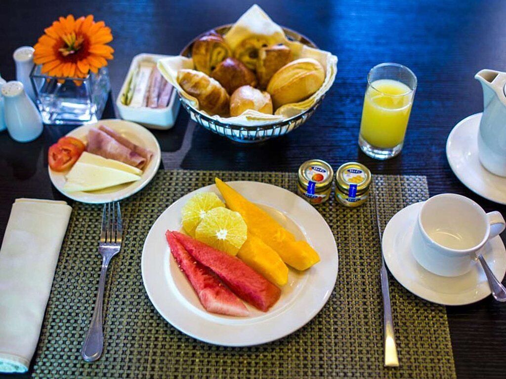 A breakfast setting with croissants, cheese, ham, and fruits on a table with a pitcher of orange juice and condiments.
