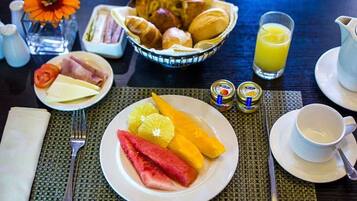 A breakfast setting with croissants, cheese, ham, and fruits on a table with a pitcher of orange juice and condiments.