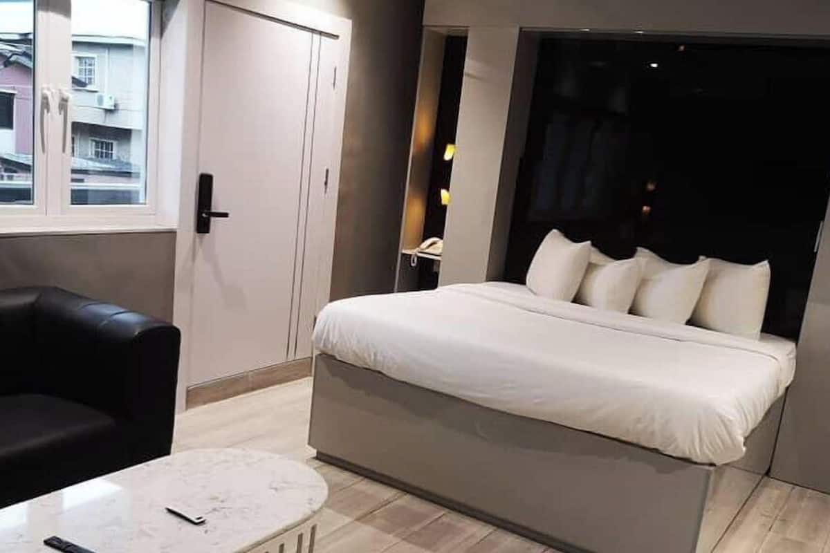 A modern hotel room with a large bed, a small round table, and a black leather chair.