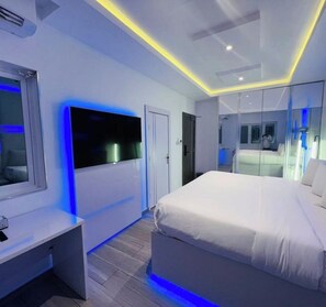Ein modernes Schlafzimmer mit einem großen Bett, einem an der Wand montierten Fernseher und einem Schreibtisch mit Stuhl.