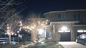 Une maison d’habitation avec une façade en pierre, un garage et une cour avant bien éclairée, décorée de guirlandes lumineuses.