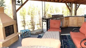 Une terrasse extérieure dotée d’une cheminée en pierre, de meubles en osier et d’un espace barbecue.