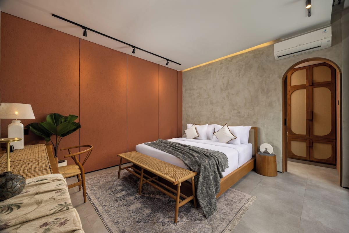 A modern bedroom with a large bed, a bench, a desk, and a potted plant.