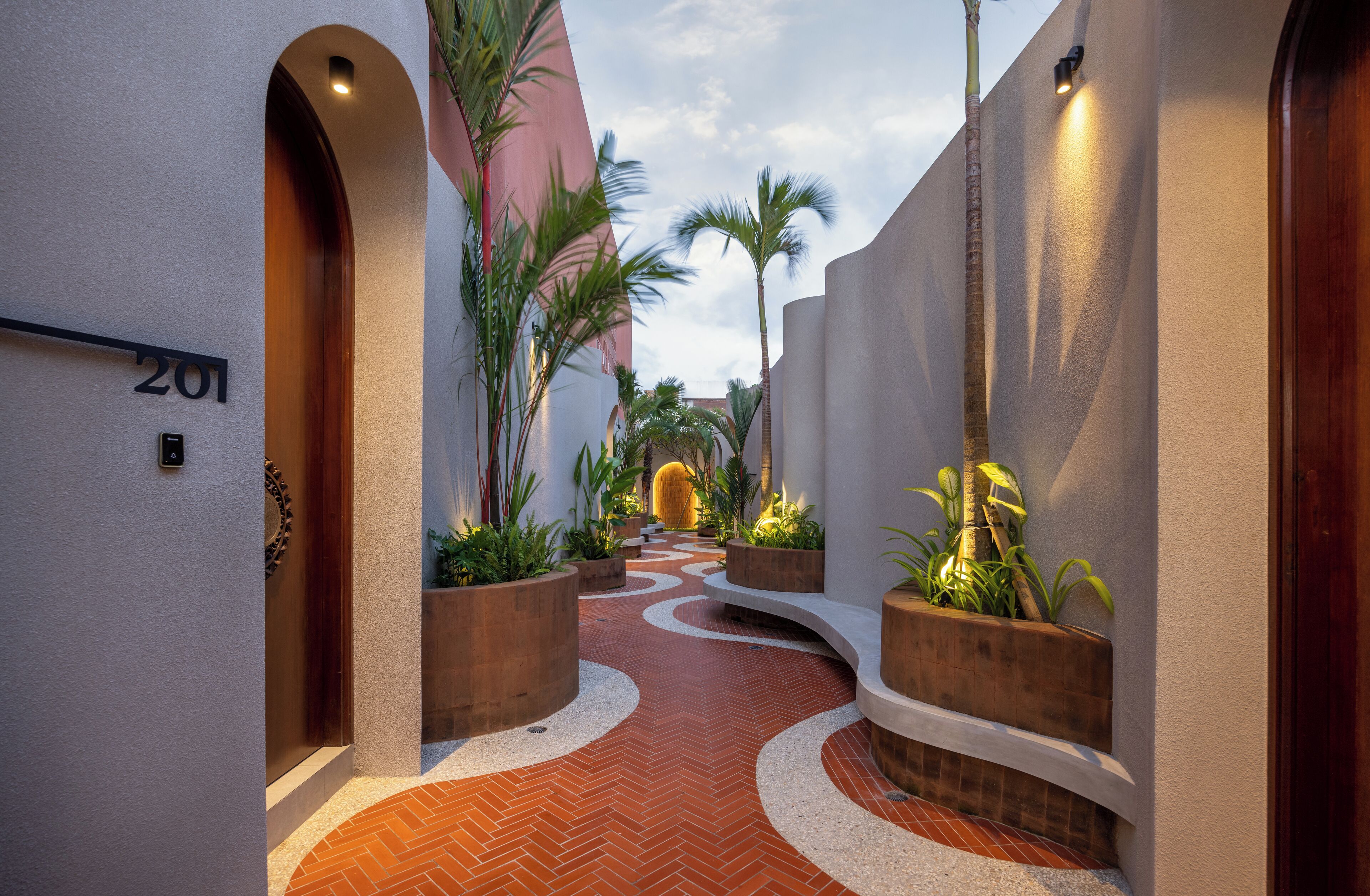 A narrow, curved pathway with a herringbone tile pattern leading to a building entrance.