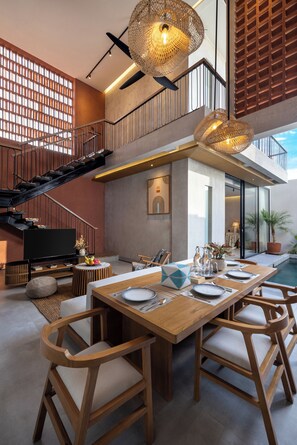 A spacious living area with a wooden dining table, comfortable seating, a staircase, and a large window providing natural light. - Terra Villas Canggu (Canggu)