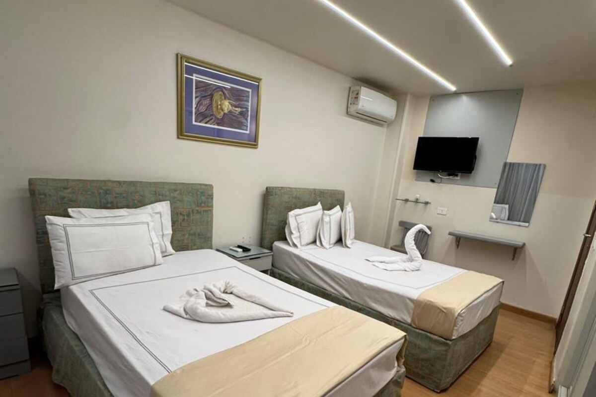 A hotel room with two beds, a flat-screen TV, a mounted air conditioner, and a framed picture on the wall.