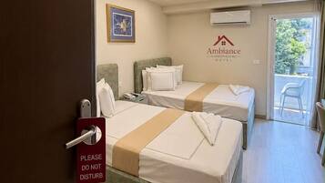 A hotel room with two beds, a door with a 'Please Do Not Disturb' sign, a wall-mounted air conditioner, and a view of the outdoors.