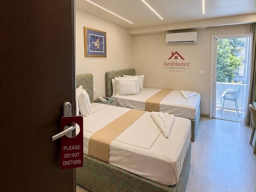 Quarto de hotel com duas camas, uma porta com a placa 'Não Perturbe' e ar-condicionado na parede, além de vista para o exterior.