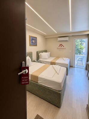 Une chambre d’hôtel avec deux lits, une porte sur laquelle est accrochée une pancarte indiquant « Veuillez ne pas déranger », un climatiseur fixé au mur et une vue sur l’extérieur.