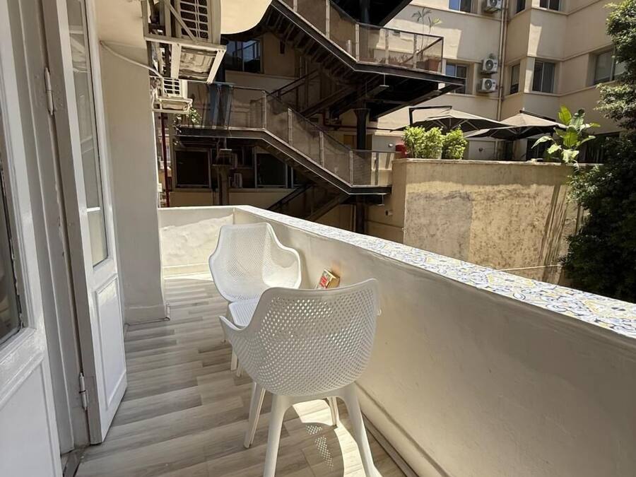 A balcony with a white chair, a wooden floor, and a view of a multi-story building with balconies and staircases.