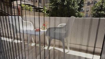 Une vue à travers une fenêtre munie d’un moustiquaire métallique, montrant une rue bordée de voitures garées et des bâtiments en arrière-plan.