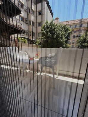 Blick durch ein Fenster mit einem Metallgitterrollo auf eine Straße mit parkenden Autos und Gebäuden im Hintergrund.