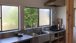A modern kitchen with stainless steel appliances, a double sink, and large windows offering a view of greenery outside. - Ichi to Koji (Gojome)