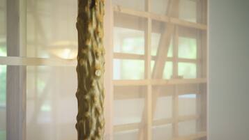 A close-up of a textured sculpture in a room with a large window and a grid-like structure in the background.