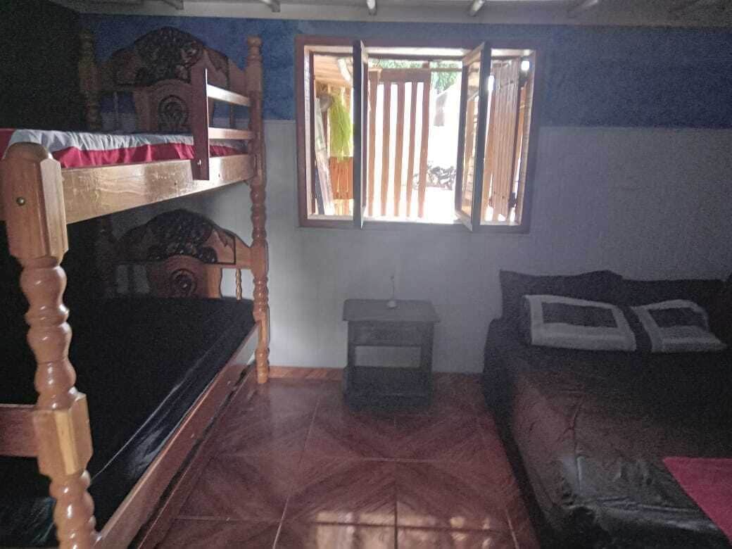 Quarto com beliche, sofá, mesa pequena e janela com venezianas verticais.